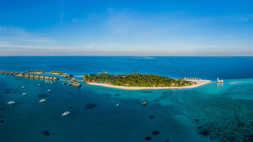 An aerial view of a tropical island with clear blue waters, a sandy beach, and a pier extending into the sea.