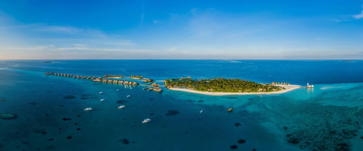 An aerial view of a tropical island with clear blue waters, a sandy beach, and a pier extending into the sea.