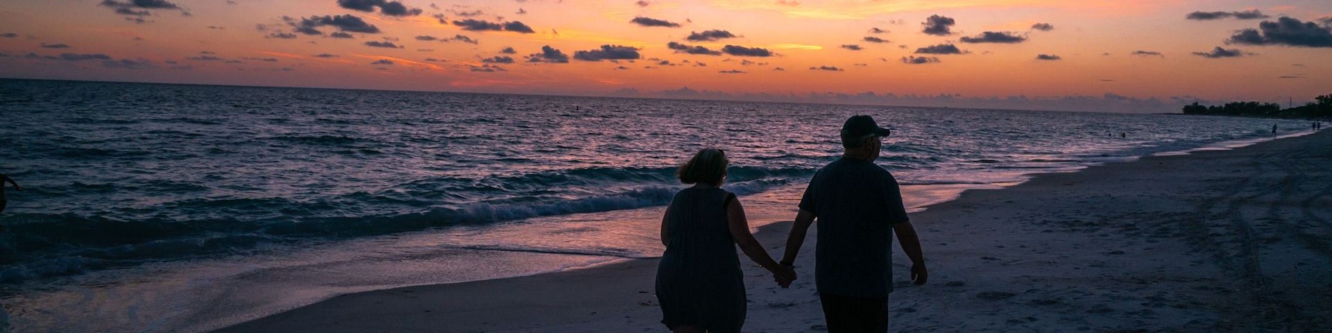 Una pareja caminando por la playa al atardecer, con un cielo lleno de colores.