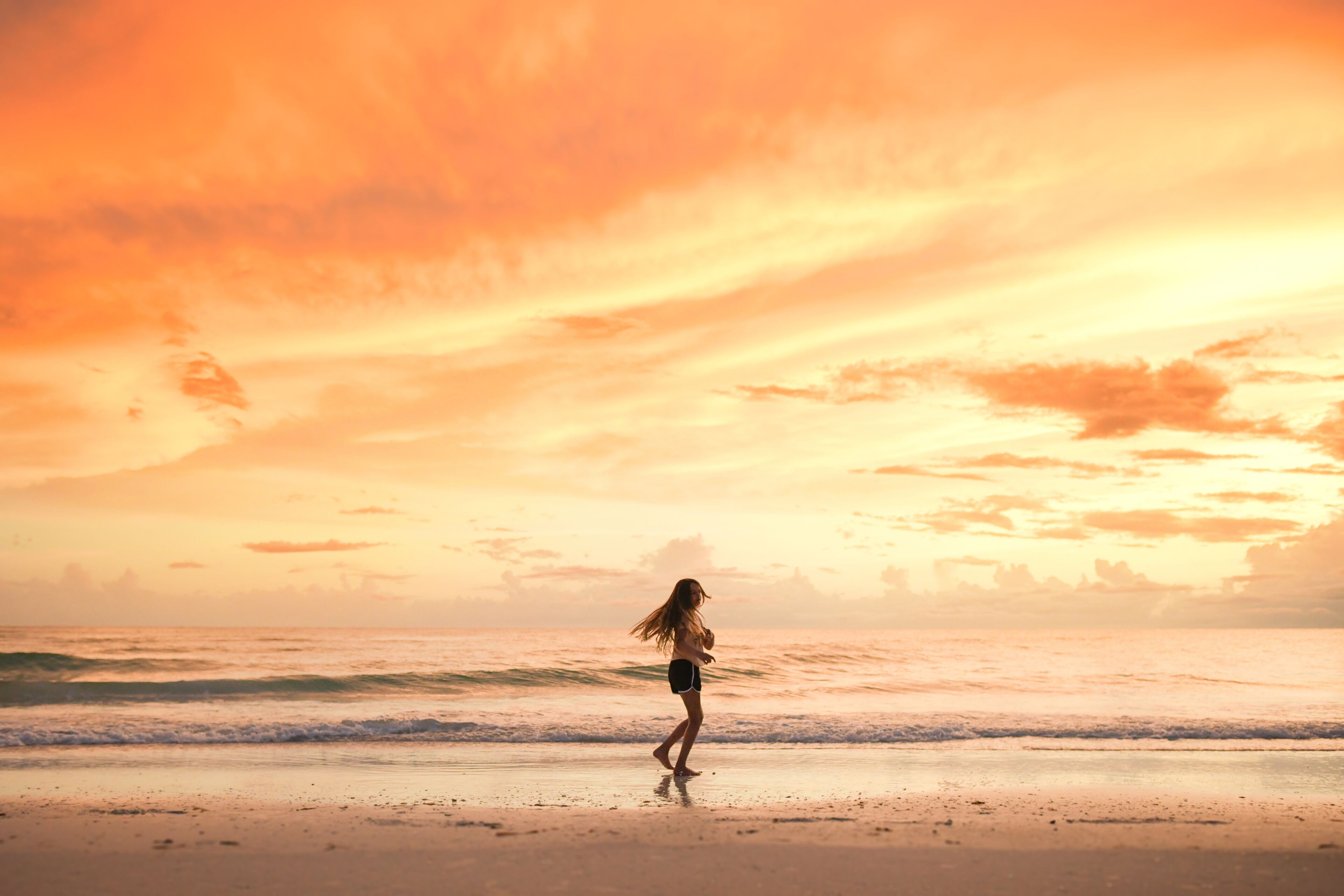 A person walking on a beach during sunset with a vibrant sky.
