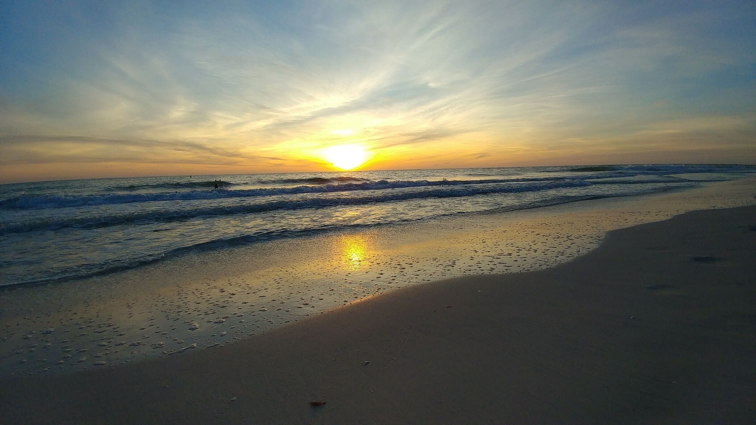 A beach with waves and a setting sun.