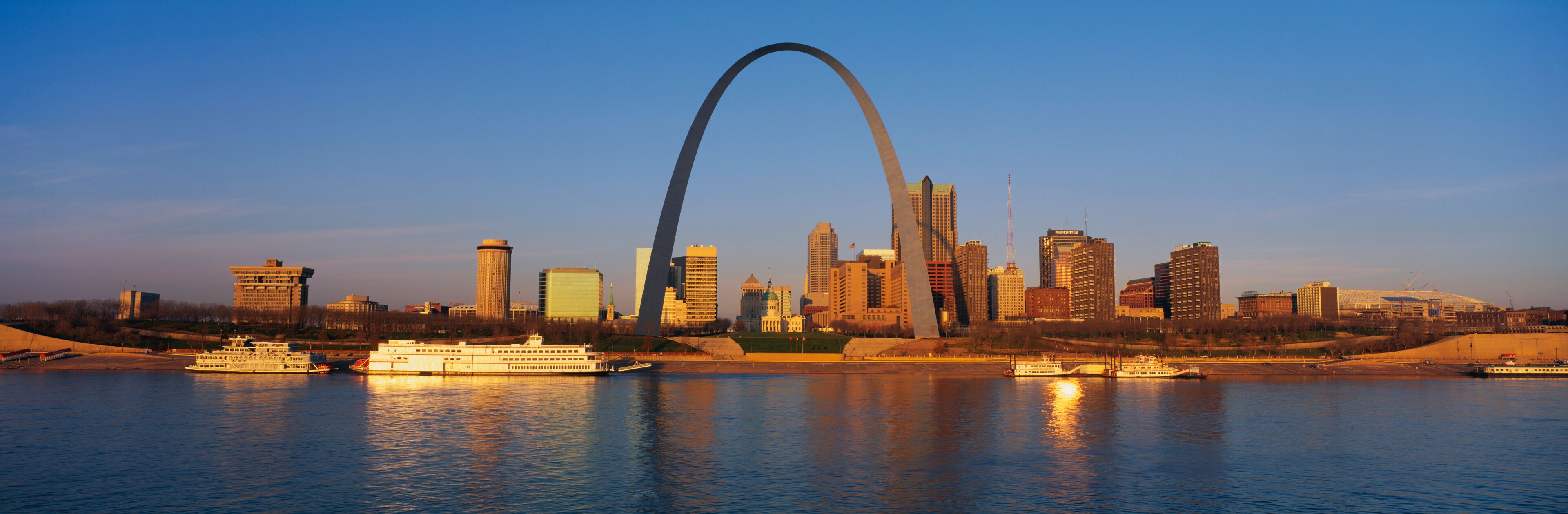 A city skyline with a prominent arch landmark, several high-rise buildings, and boats on a river.