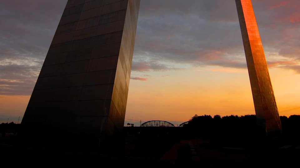 A large arch structure with a lit interior, set against a sunset sky.