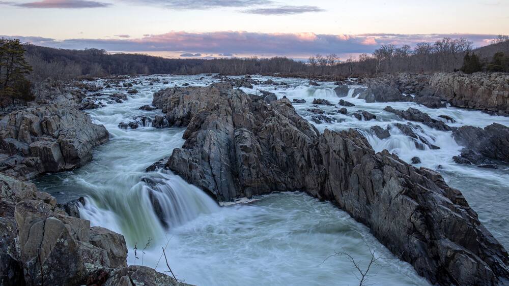 A river with a waterfall surrounded by rocky terrain and a forested landscape.