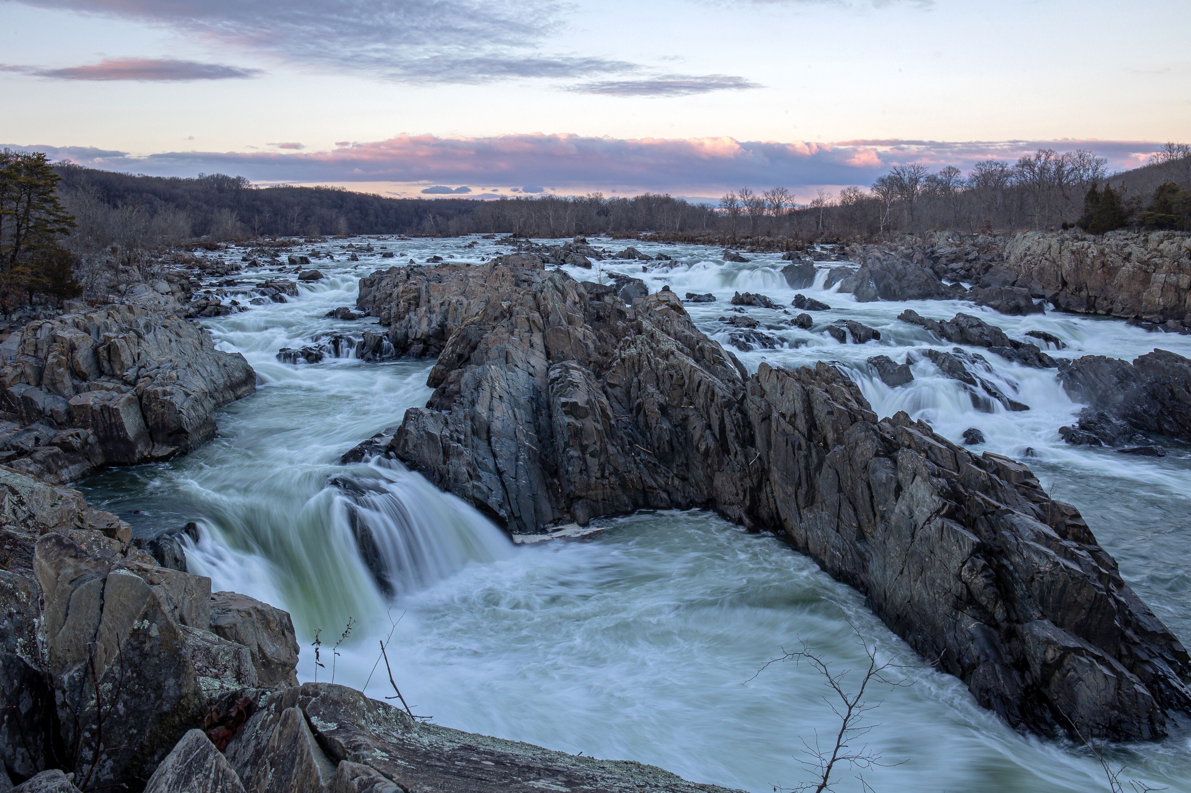 A river with a waterfall surrounded by rocky terrain and a forested landscape.
