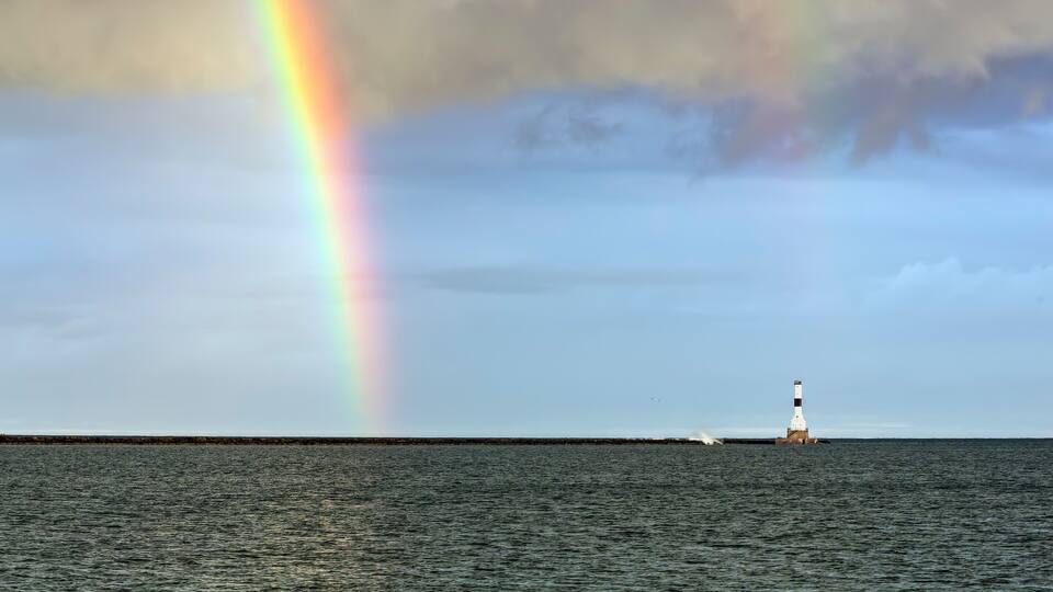 A lighthouse on a pier with a rainbow in the sky.