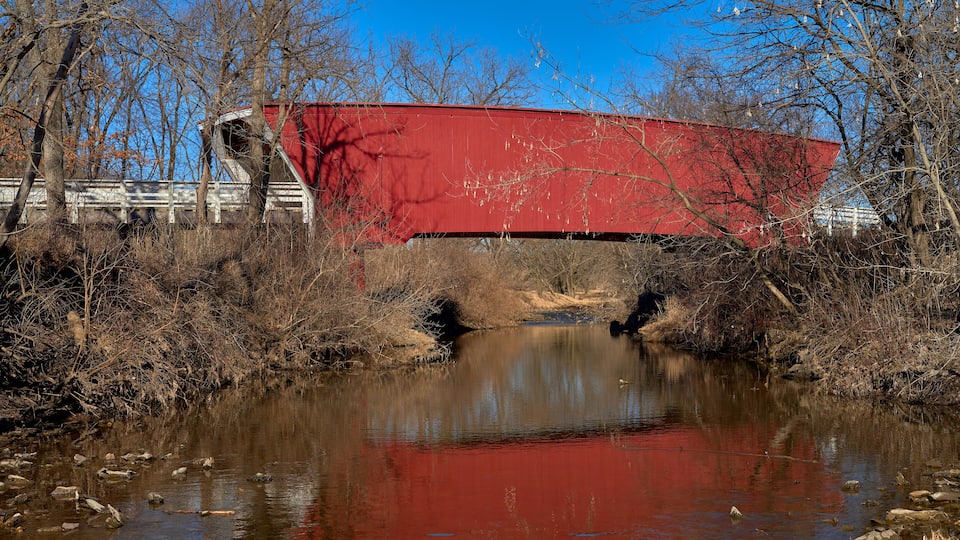 A red bridge over a calm river with trees and a clear blue sky in the background.
