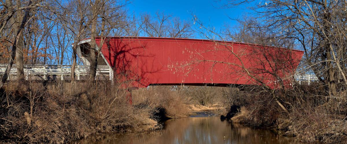 A red bridge over a calm river with trees and a clear blue sky in the background.
