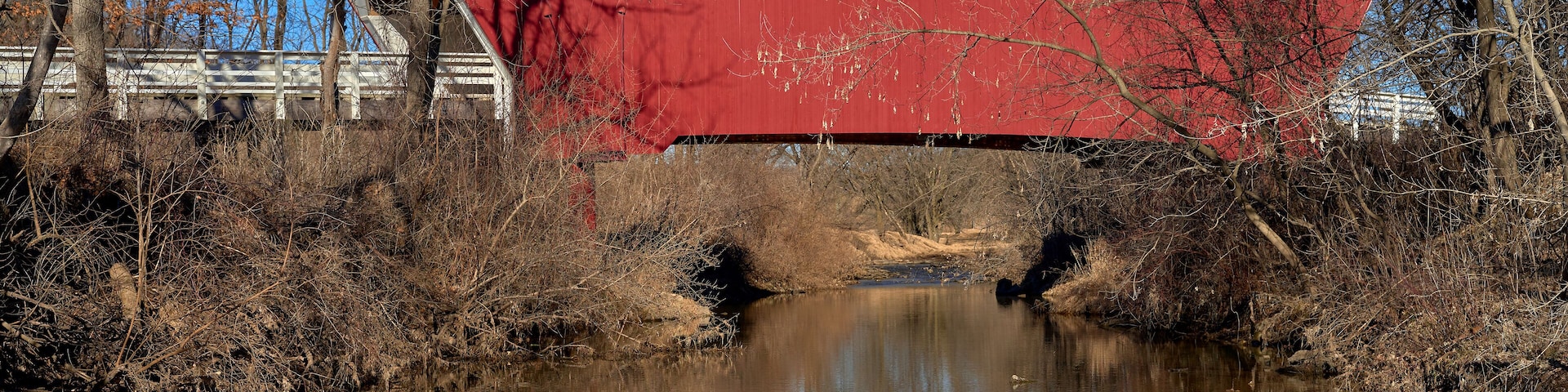 A red bridge over a calm river with trees and a clear blue sky in the background.