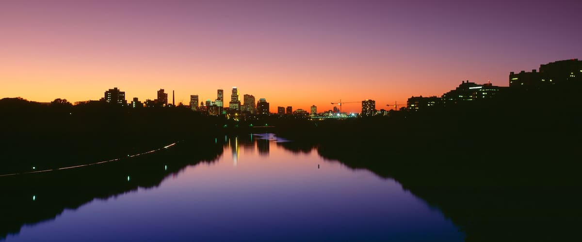 A city skyline at dusk with a river reflecting the lights.