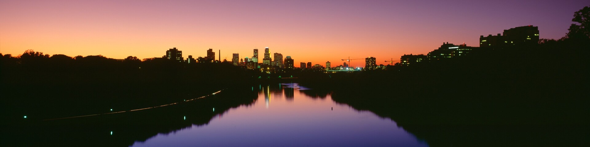 A city skyline at dusk with a river reflecting the lights.