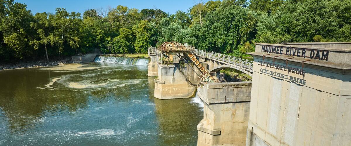 A dam with a bridge, water flow, and surrounding greenery.