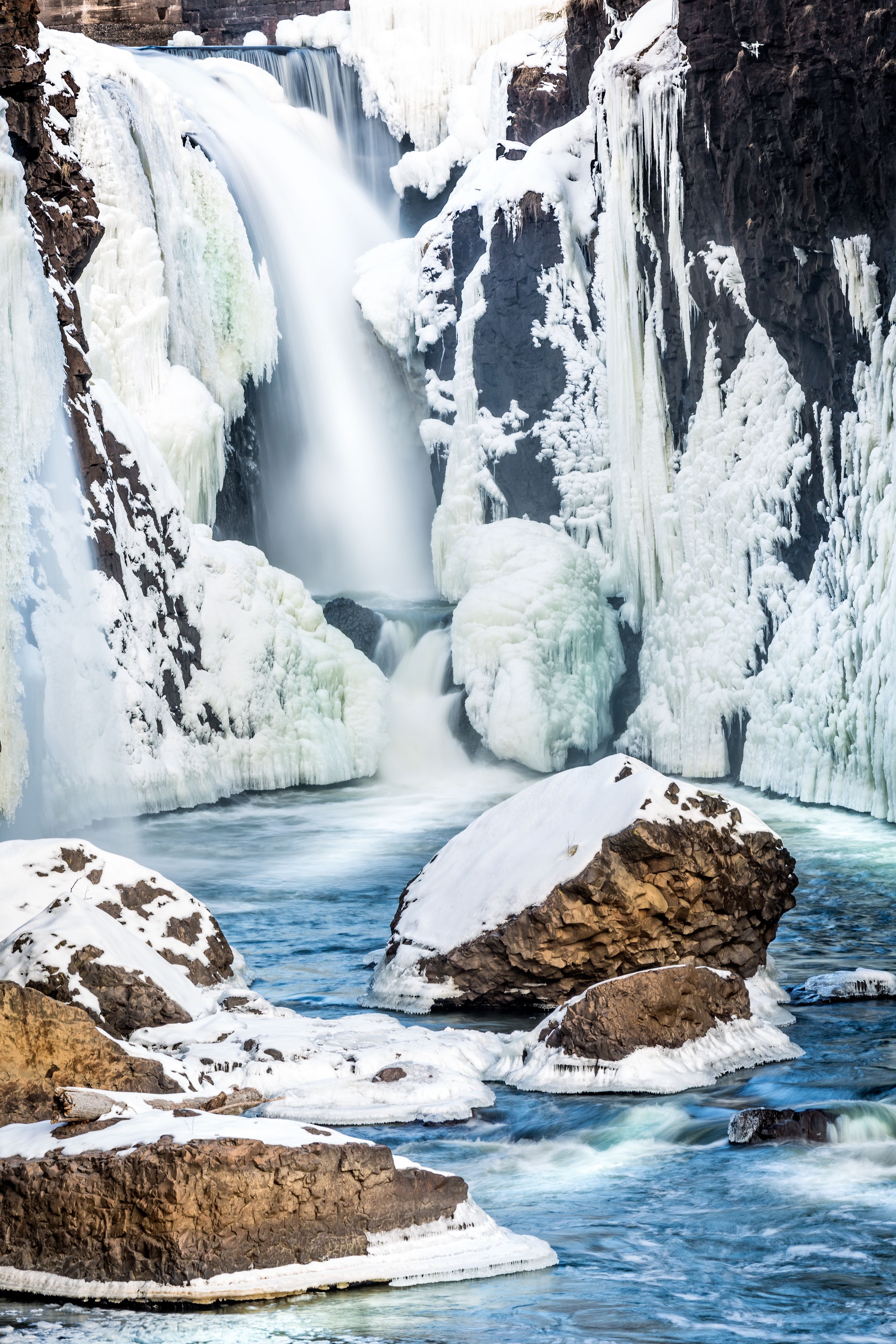 A frozen waterfall surrounded by snow-covered rocks and ice formations.