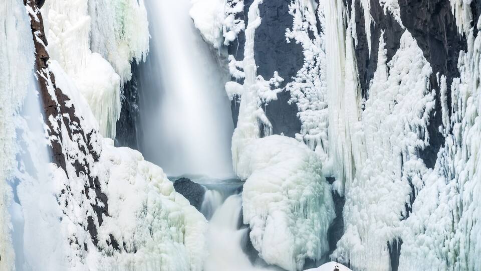 A frozen waterfall surrounded by snow-covered rocks and ice formations.