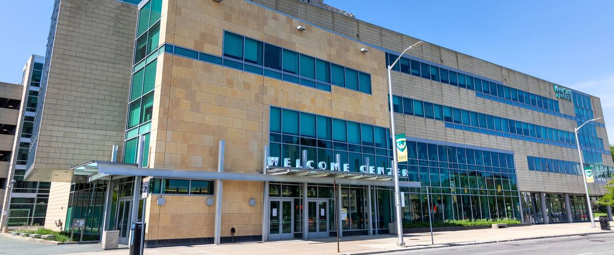 Un edificio moderno con señalización de 'Wayne State University', entrada al 'Welcome Center' y un cielo azul despejado.