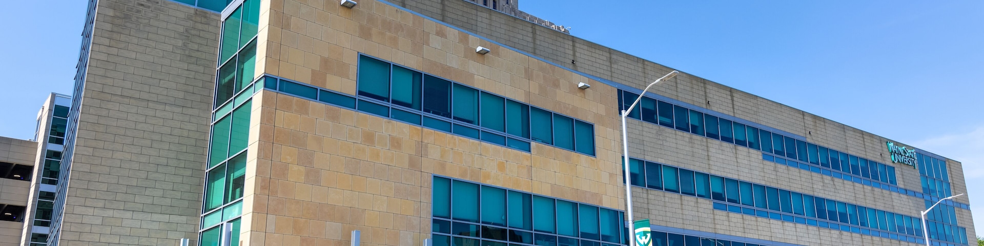 Ein modernes Gebäude mit der Beschilderung 'Wayne State University', einem Eingang zum 'Welcome Center' und blauem, wolkenlosem Himmel.