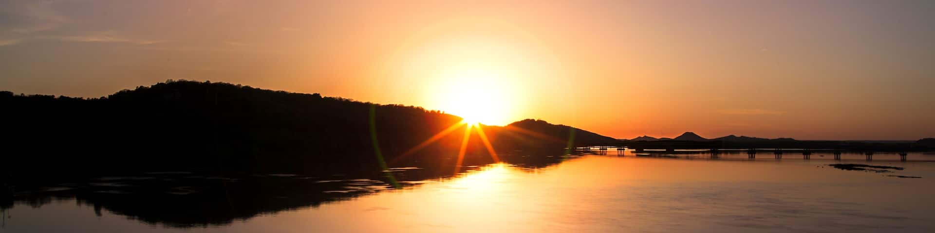 A sunset over a calm lake with a pier extending into the water.