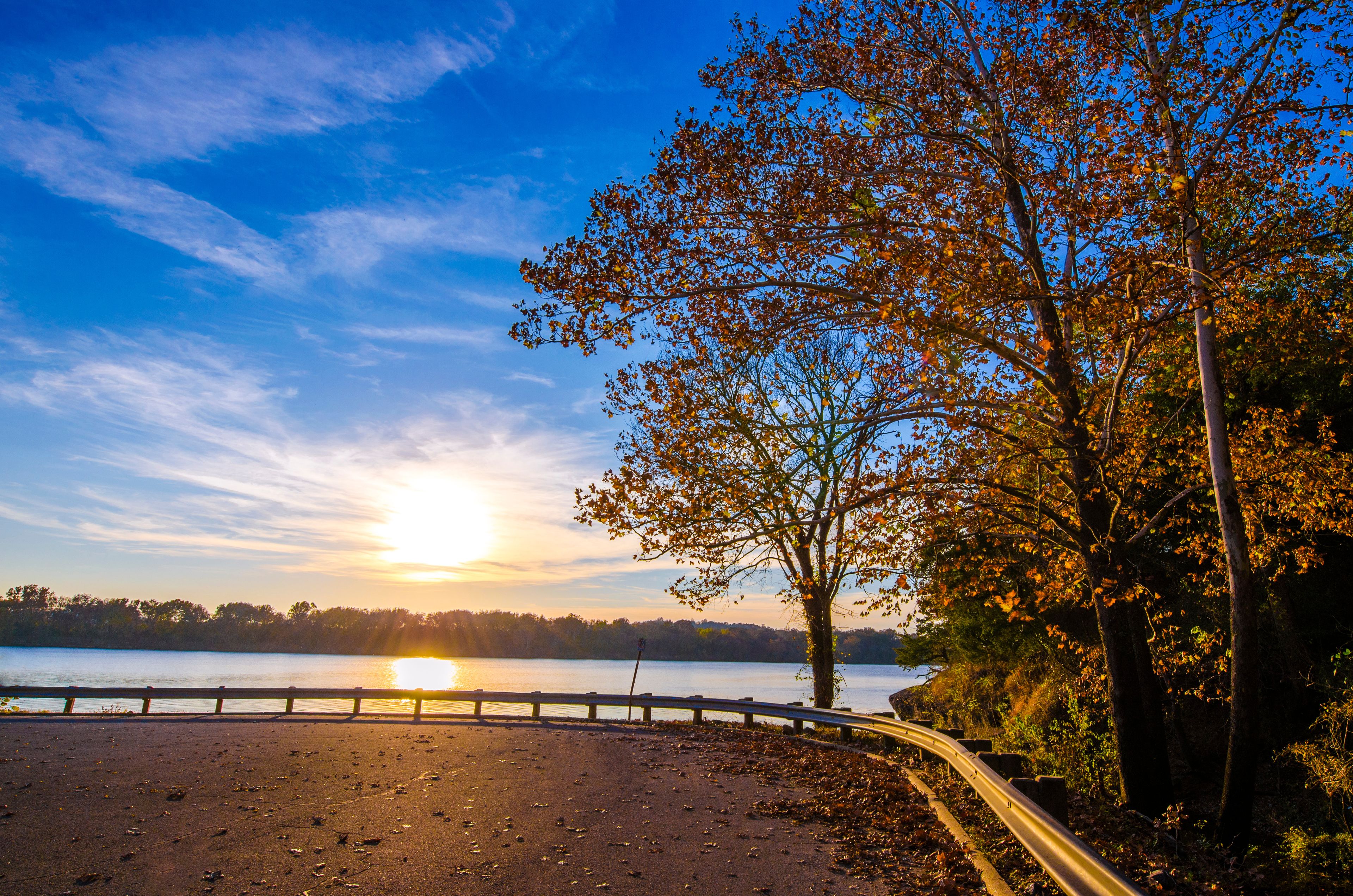 A sunset over a lake with a curved road and trees.
