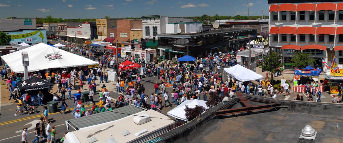 A crowded street festival with tents and a large crowd.