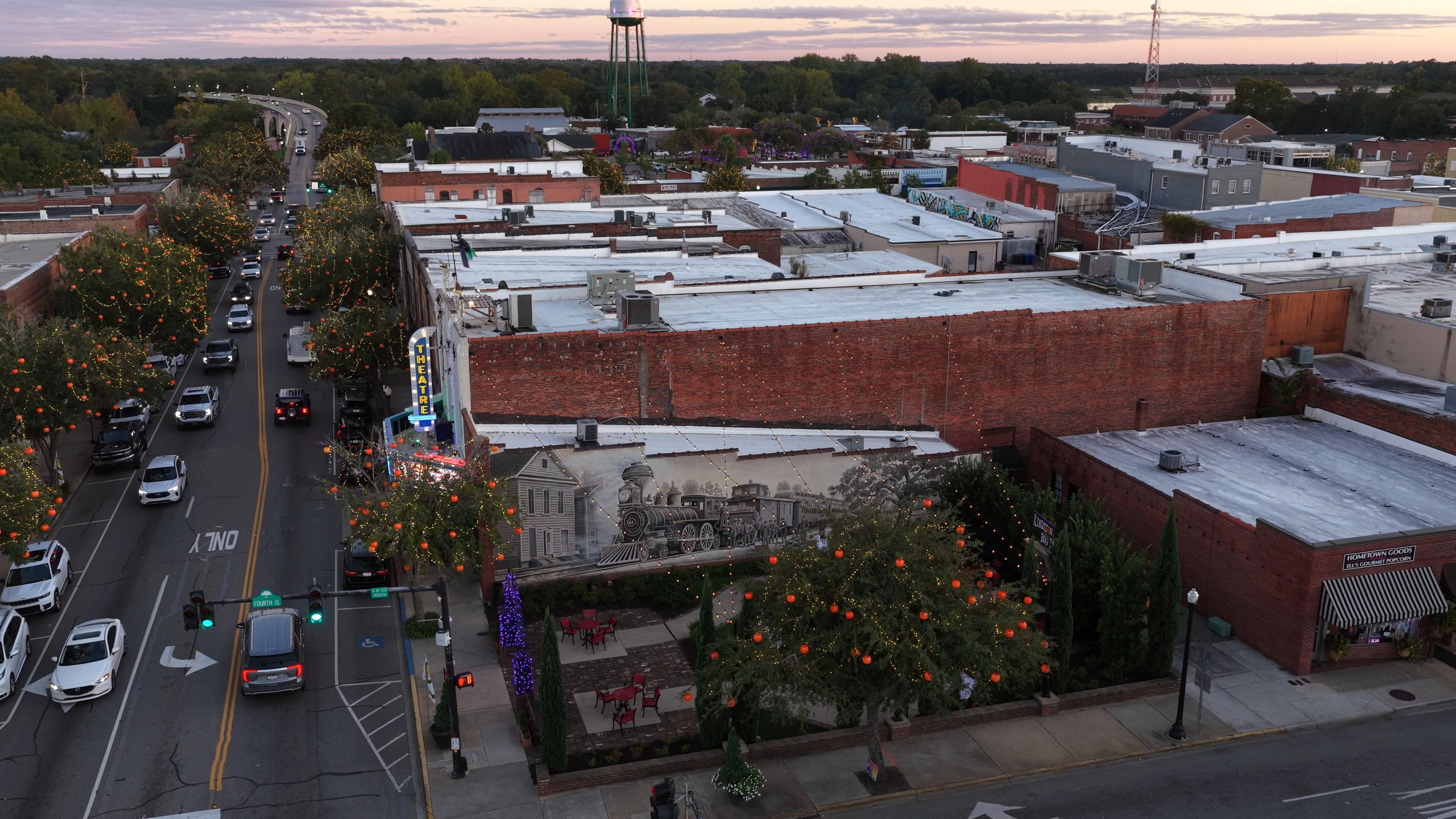 A city street lined with trees decorated with lights, a theater, and a brick building with a sign for a popcorn stand.