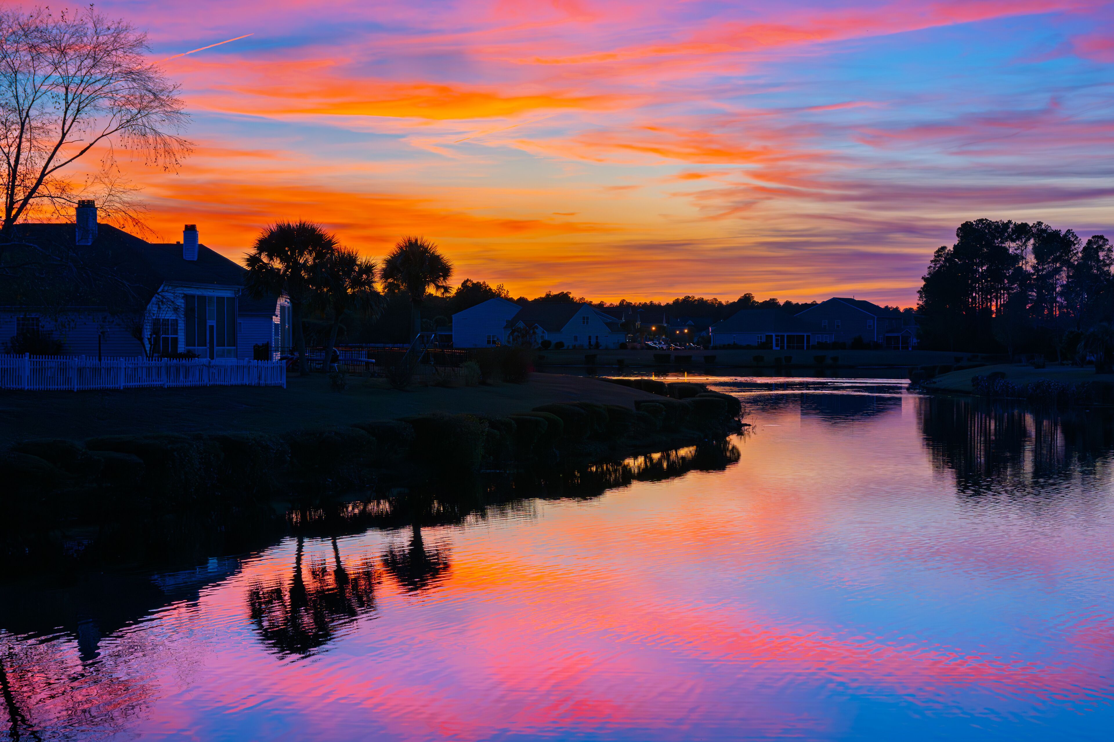 A small lake in a suburban neighborhood reflects a colorful sunset in the Conway Myrtle Beach area of South Carolina.