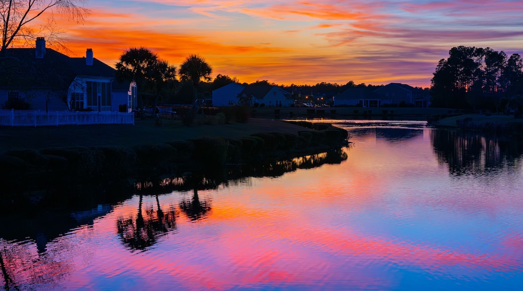 A small lake in a suburban neighborhood reflects a colorful sunset in the Conway Myrtle Beach area of South Carolina.