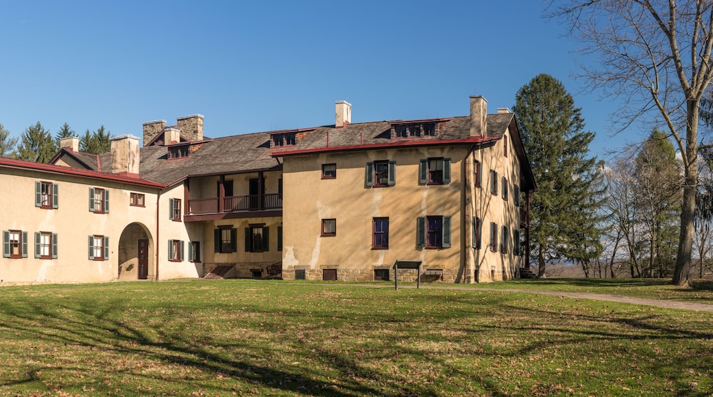 A large, historic building with multiple chimneys and a red roof, surrounded by a grassy area and trees.