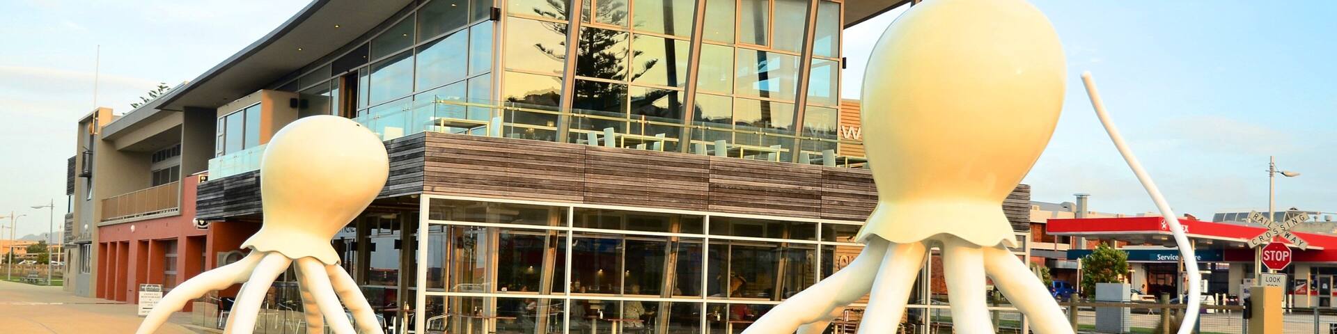 A modern building with glass windows and a large sculpture of two octopuses in a water feature.