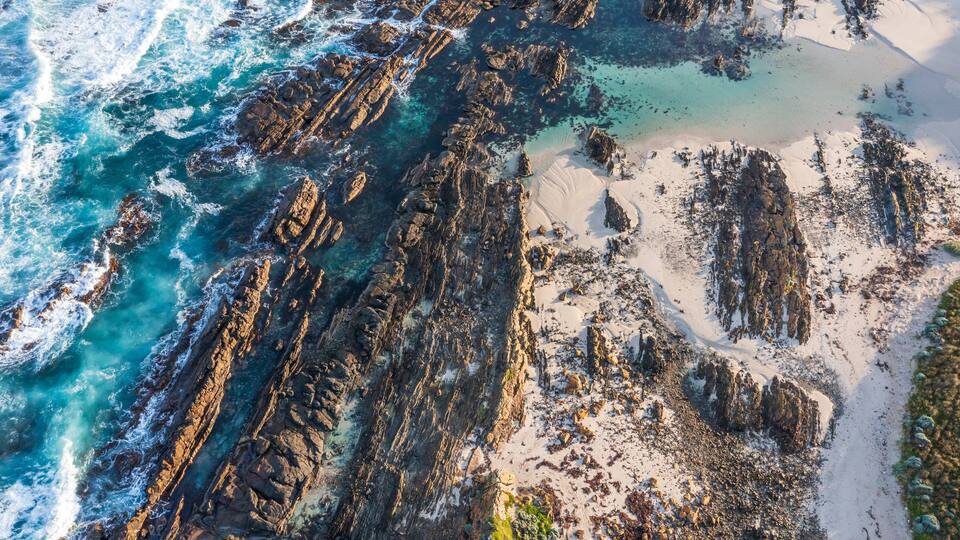 A coastal landscape with rocky cliffs, clear turquoise waters, and sandy beaches.