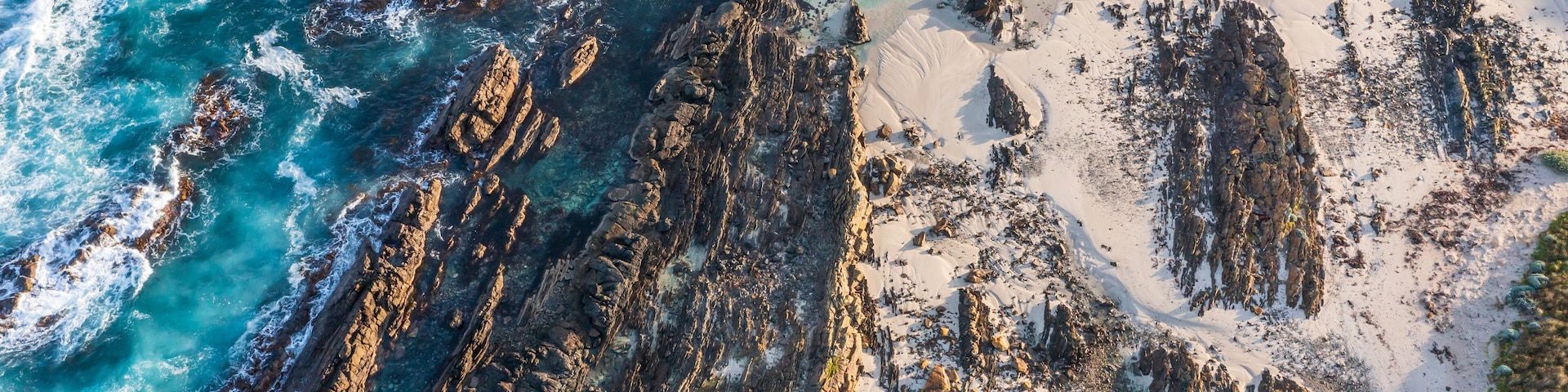 A coastal landscape with rocky cliffs, clear turquoise waters, and sandy beaches.