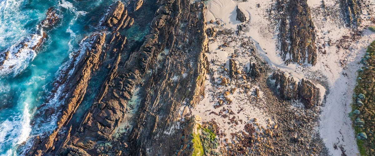 A coastal landscape with rocky cliffs, clear turquoise waters, and sandy beaches.