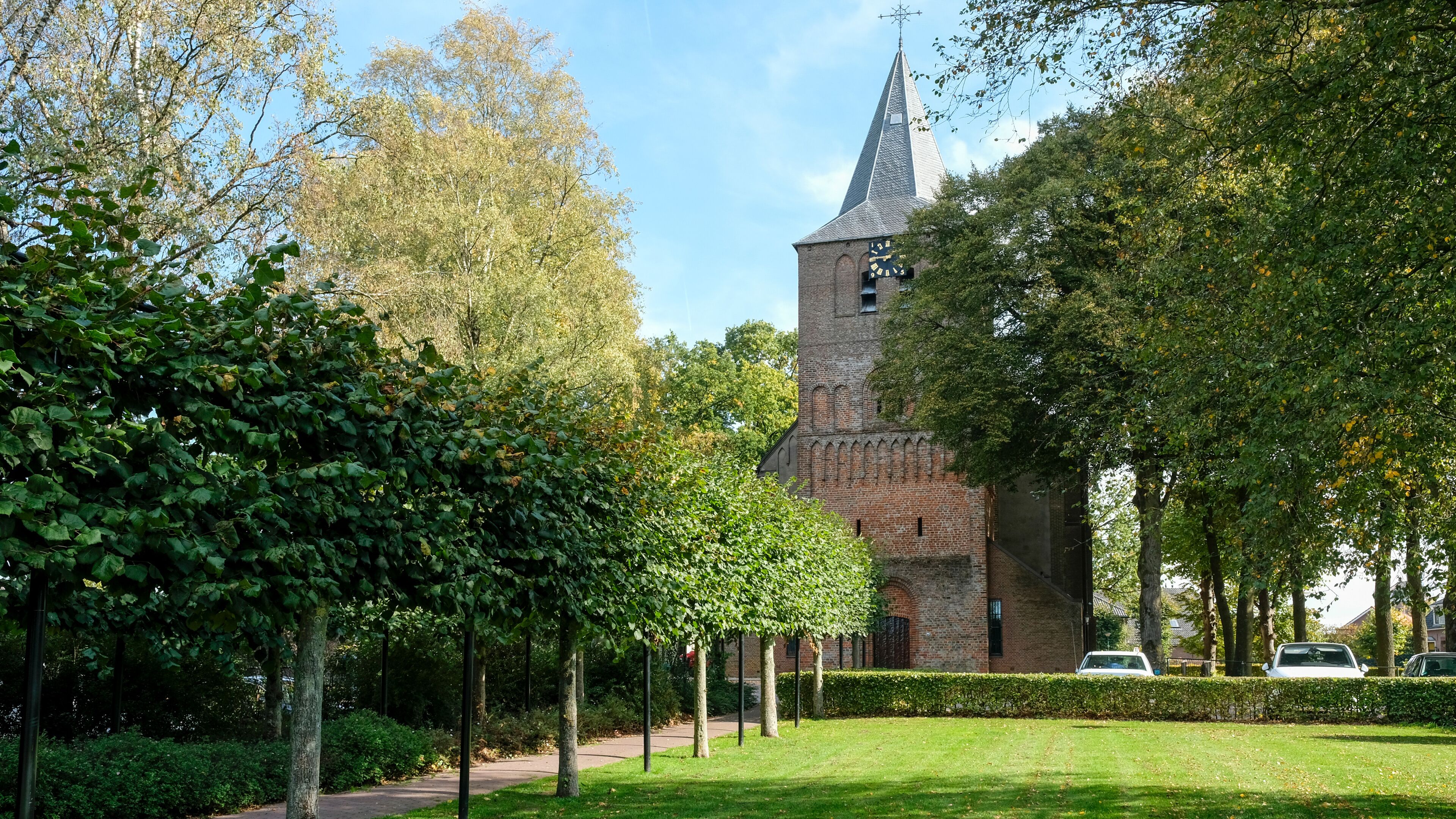 A historic church with a tall tower and a clock, surrounded by lush greenery and trees.