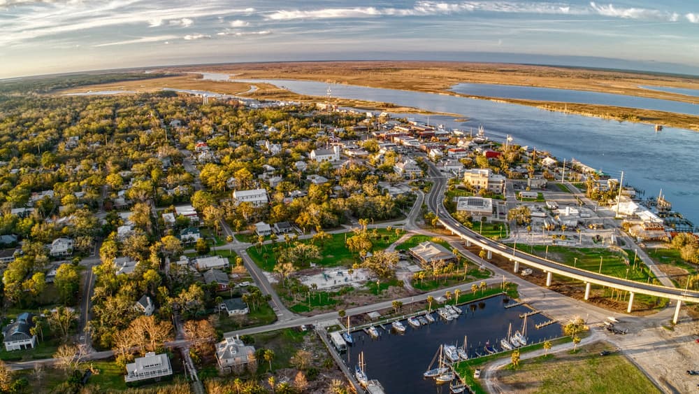 An aerial view of a coastal town with a marina, a bridge, and surrounding water bodies.