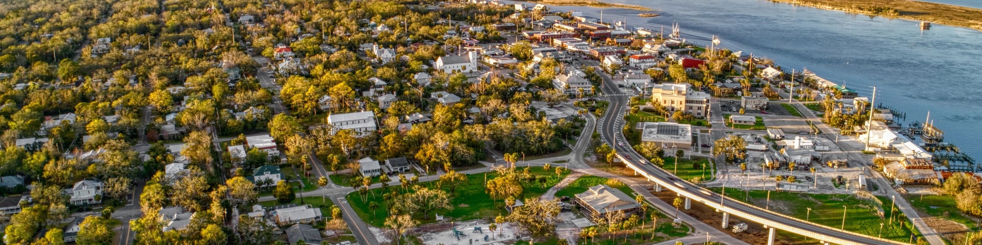 Vista aérea de uma cidade costeira com um porto, uma ponte e corpos d'água ao redor.