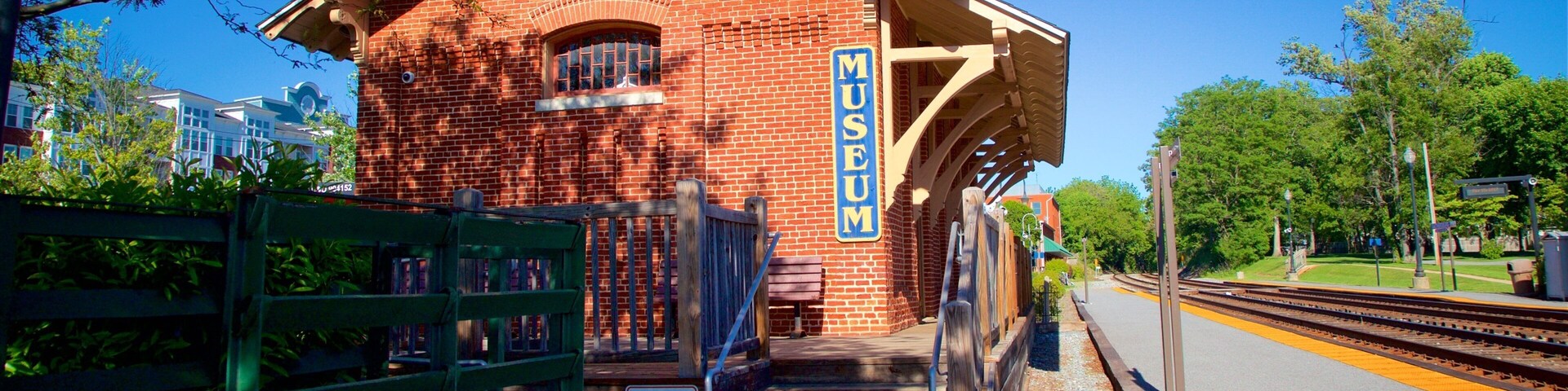 A brick building labeled "FREIGHT HOUSE MUSEUM" with a covered platform and a green cart.