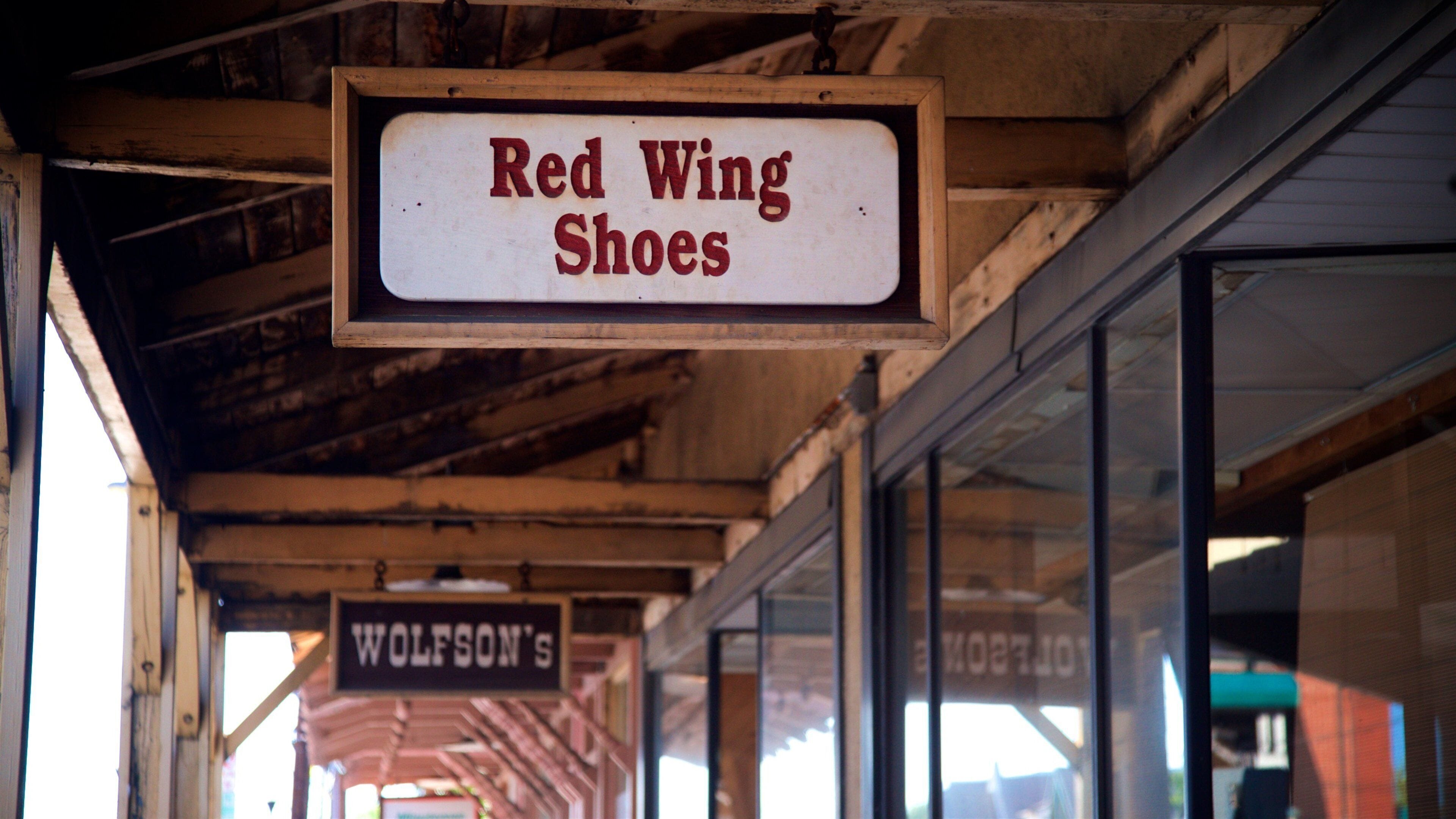 A sign for 'Red Wing Shoes' hanging from a wooden structure.