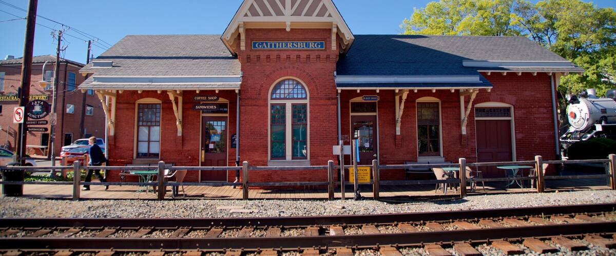 A red brick train station with a sign reading "Gaithersburg" and a steam locomotive in the background.
