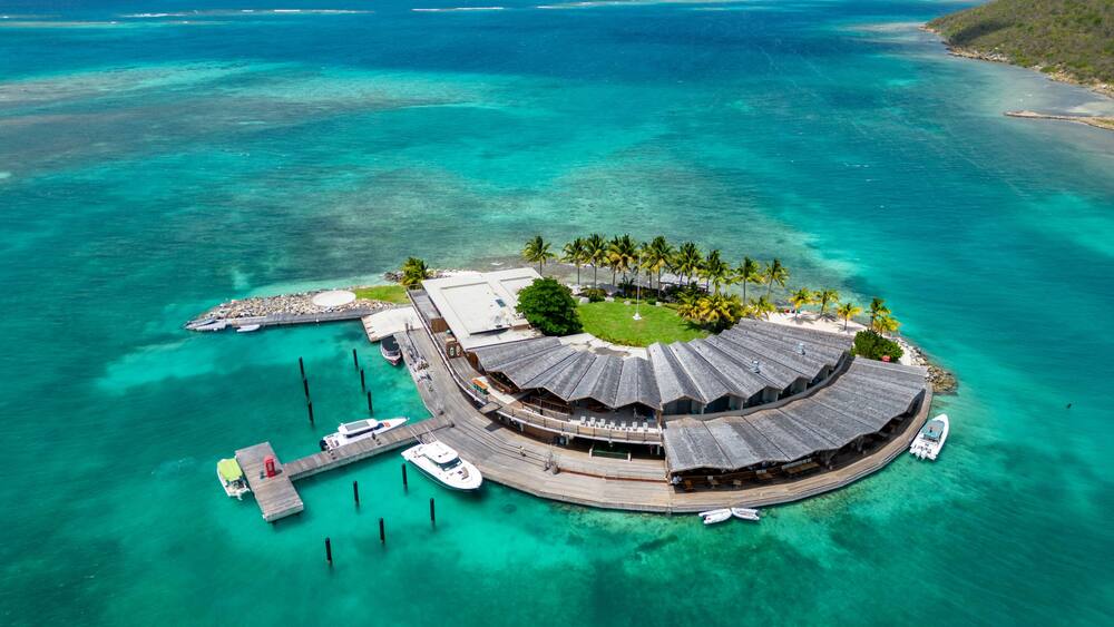 A tropical island with a circular building surrounded by palm trees and clear turquoise waters.