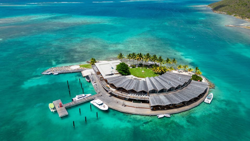 A tropical island with a circular building surrounded by palm trees and clear turquoise waters.