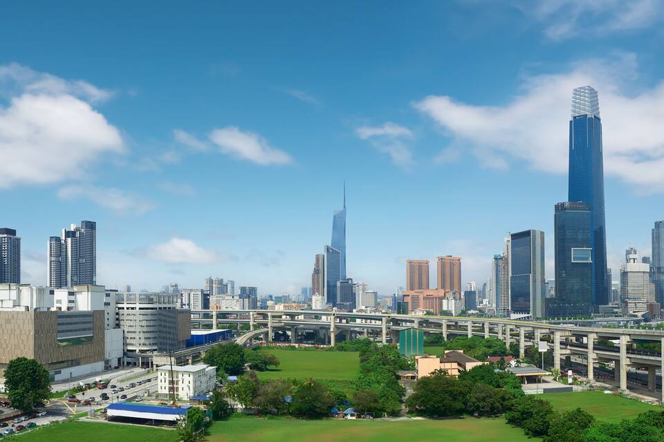 Paisagem urbana com arranha-céus modernos, incluindo um edifício alto e imponente com design singular, e uma autoestrada elevada.