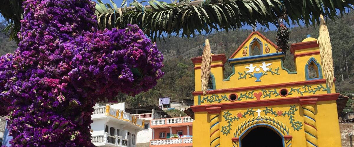 A colorful church with a yellow facade and a purple flowering tree in the foreground.