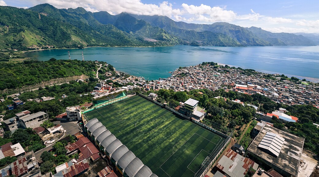 Aerial view of a soccer field nestled between lush greenery and the tranquil waters of Lake Atitlan, with homes cascading down the hillside, Antigua Guatemala, Sacatepequez Department, Guatemala.