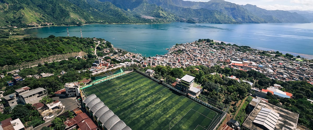 Una cittadina costiera con un grande campo da calcio, montagne e un lago tranquillo.