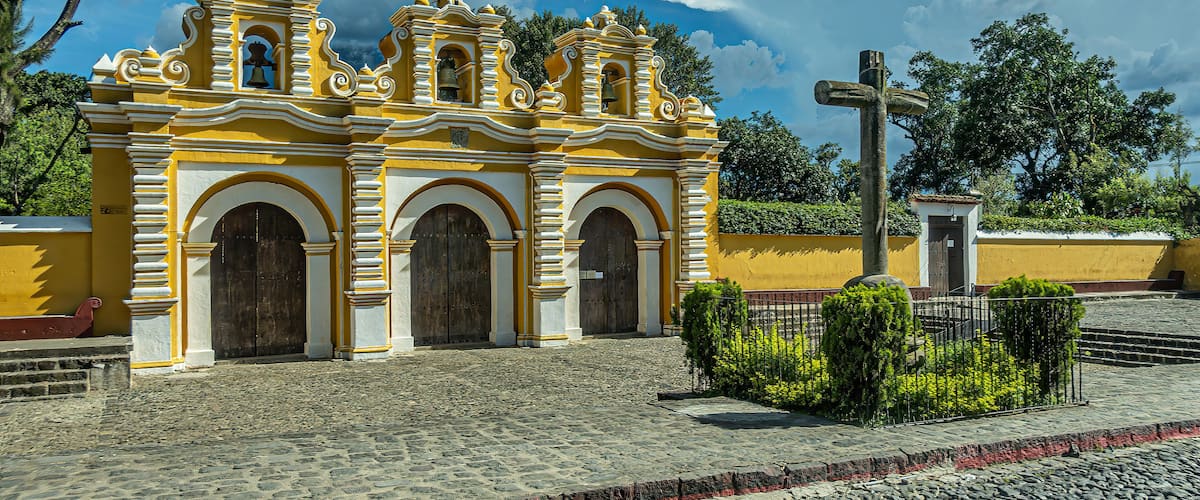 Una chiesa coloniale gialla e bianca con una croce di fronte.