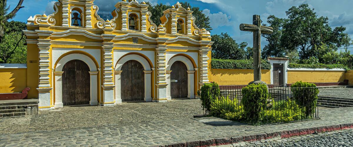A yellow and white colonial church with a cross in front.