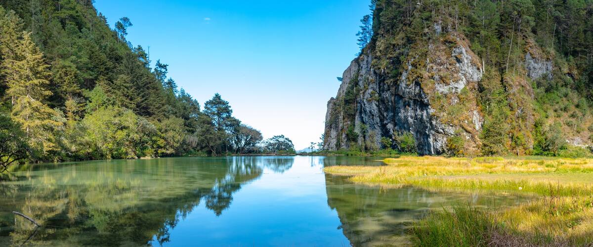 A calm river flanked by dense forests and rocky cliffs.