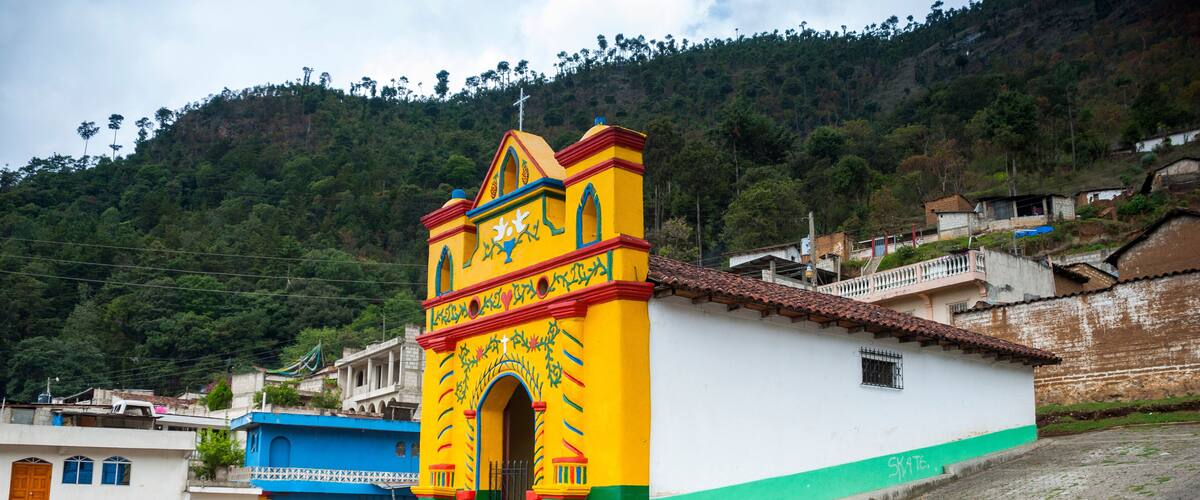 A colorful church with a bell tower, steps leading up to it, and a hillside in the background.
