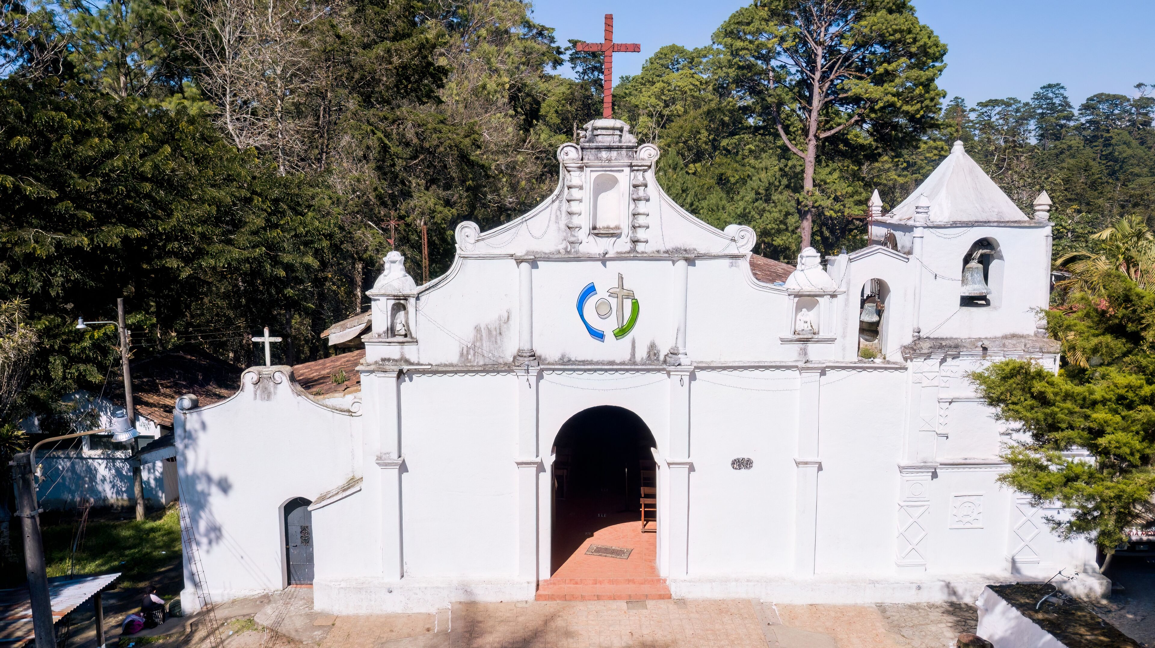 A white church with a cross on top, a bell tower, and a large archway.