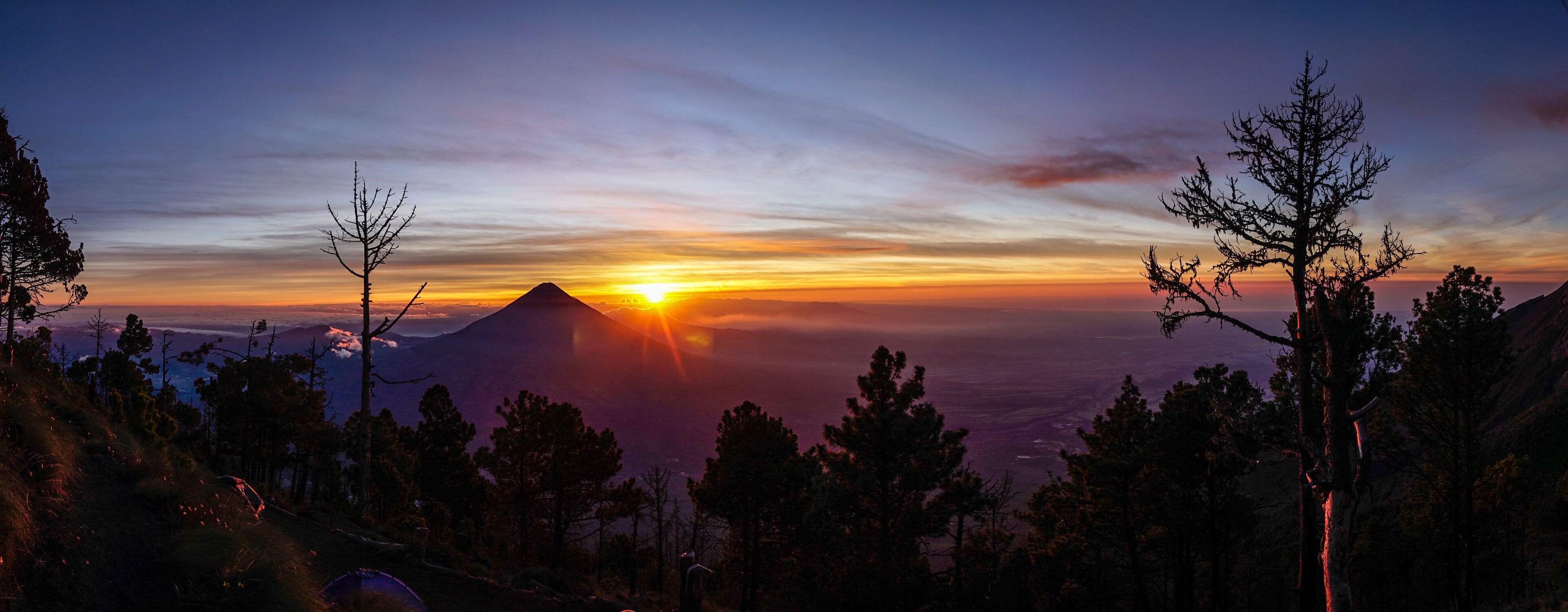 A mountain at sunset with a clear sky and silhouetted trees.
