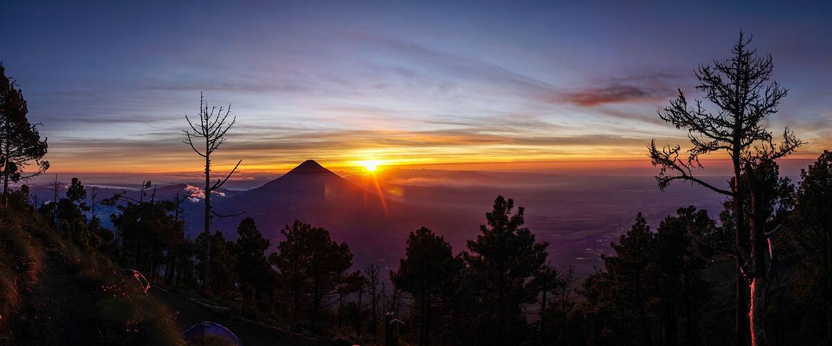 A mountain at sunset with a clear sky and silhouetted trees.